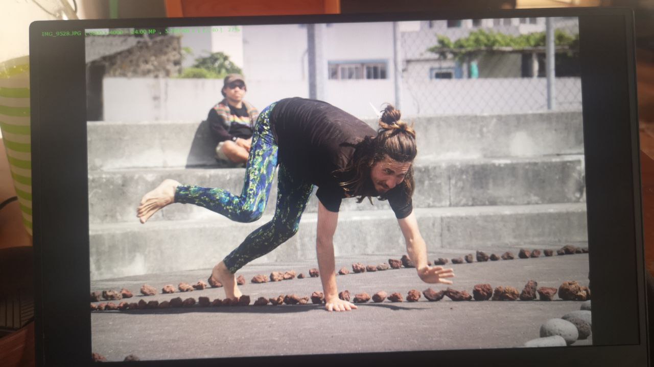 Michal in green leggings and on all fours, jumping above a line made of small rocks